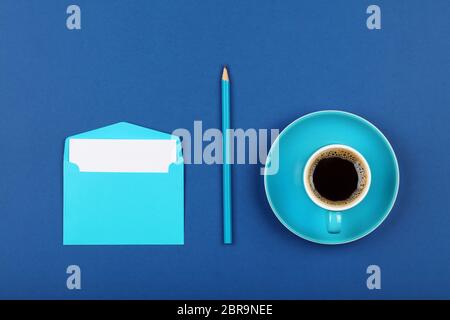 Eine offene leere Pastell-blaue Umschlag mit weißen Papier, schwarz Kaffee Tasse und Holz Bleistift über Dark indigo blauen Hintergrund, Flach, direkt über Stockfoto