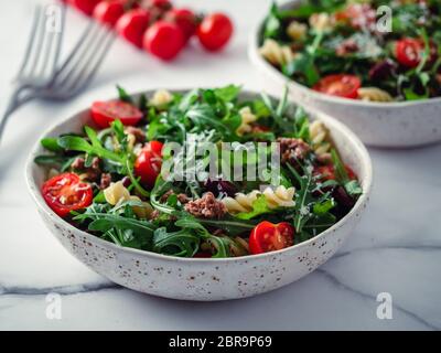 Warmer Salat mit Thunfisch, Rucola, Tomaten, roten Bohnen, Nudeln. Idee und Rezept für gesundes Mittag- oder Abendessen. Zwei Schüsseln mit warmen Salaten auf Marmor Tischplatte. Stockfoto