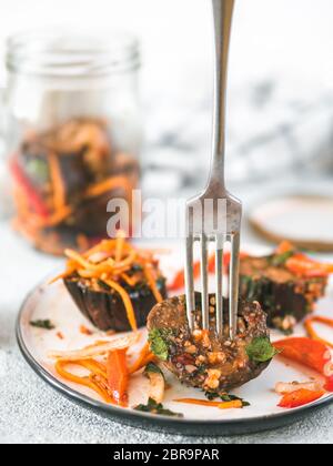 Salat eingelegte Auberginen, Möhren, Zwiebeln, Paprika auf Platte über Grauzement Hintergrund. Gabel in erhaltenen Aubergine Slice. Glas Glas mit konserve auf b Stockfoto