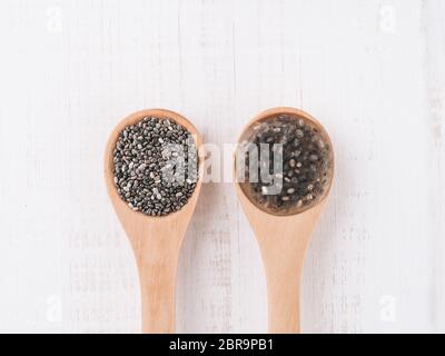 Trockene Chiasamen und nasse Chiasamen oder Chia-Ei in Holzlöffeln auf weißem Holzhintergrund. Eierersatz, pflanzliche Eier, Veganer ersetzen Eier concep Stockfoto