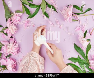 Zwei Hände eines jungen Mädchens mit glatter Haut und ein Blumenstrauß rosa Pfingstrosen auf einem lila Hintergrund, Ansicht von oben, modische Konzept für Hand Hautpflege, ant Stockfoto