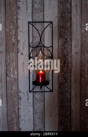 Eine brennende rote Kerze auf eine Holzwand. Stockfoto