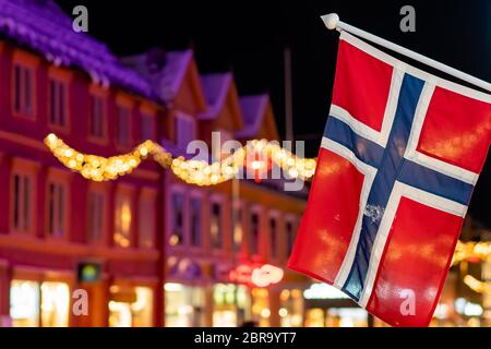 Norwegische Flagge an einem Pol in Tromso Zentrum in der Weihnachtszeit nach Einbruch der Dämmerung, Norwegen Stockfoto