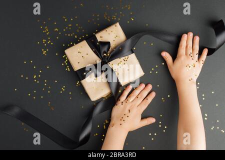 Time Geschenke - stilvolle Geschenkbox und Kinder Hände mit goldenen Stern Konfetti auf schwarzem Tisch. Magic stilvolle Urlaub Hintergrund, schwarzer freitag, Sale Coupon, Weihnachten Stockfoto