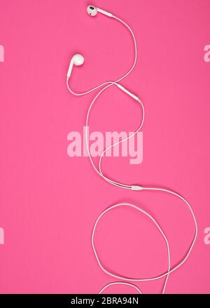 Ohrhörer mit einem weißen Kabel auf einem rosa Hintergrund, abstrakt Hintergrund Stockfoto