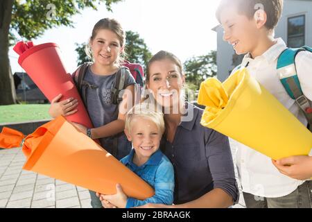 Fröhliche Frau und Kinder am Einschreibtag mit Schulzapfen Stockfoto