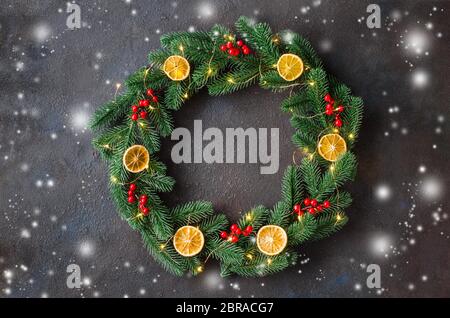 Weihnachten Baum Tür Kranz aus Tannenzweigen mit Weihnachtsbeleuchtung und Dekoration auf dunklem Hintergrund. Kopieren Sie Platz im Mittelrahmen und leeren Mock up für Stockfoto