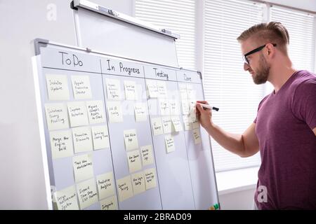 Lächelnd Geschäftsmann kleben Klebstoff Hinweis auf dem Whiteboard im Büro Stockfoto