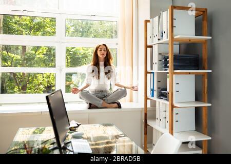 Entspannt junge geschäftsfrau Meditation in Lotus Position über Schaltschrank in der Nähe der Fenster Stockfoto