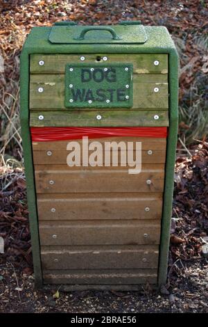 Grüne hölzerne Hundeabfallbehälter mit einem Metallrahmen im Wald. Rote Plastiktüte für die Abfallvorzeigen. Hintergrund der toten Blätter. Stockfoto