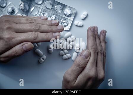 Hände decken und verstecken viele weiße verschreibungspflichtige Medikamente, Medikamente Tabletten oder Vitaminpillen in einem Haufen - Konzept der Gesundheitsversorgung, Opioide sucht, Scham, Stockfoto