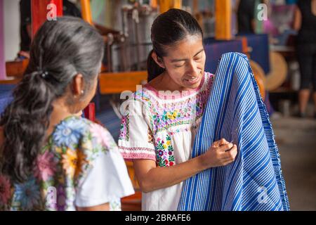 Eine Kunsthandwerkerin weist auf ein Detail bezüglich Textilmaterial in einer Kooperative in Oaxaca, Mexiko, hin. Stockfoto