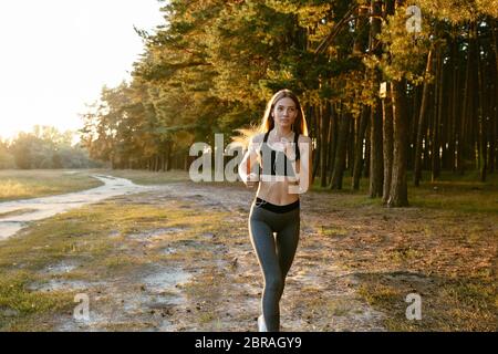 Volle Länge Foto von schönen Mädchen laufen, joggen Während outdoor Training im Holz, istening Musik in Headset. In Leggings und Tank Top gekleidet. Stockfoto