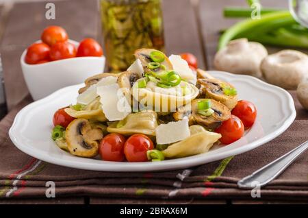 Hausgemachte Tortellini gefüllt mit Pilzen und Frühlingszwiebeln, gerösteten Tomaten, Knoblauch Souce gekrönt parmesan Stockfoto