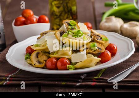 Hausgemachte Tortellini gefüllt mit Pilzen und Frühlingszwiebeln, gerösteten Tomaten, Knoblauch Souce gekrönt parmesan Stockfoto