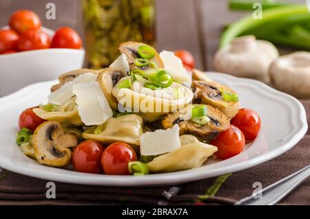 Hausgemachte Tortellini gefüllt mit Pilzen und Frühlingszwiebeln, gerösteten Tomaten, Knoblauch Souce gekrönt parmesan Stockfoto