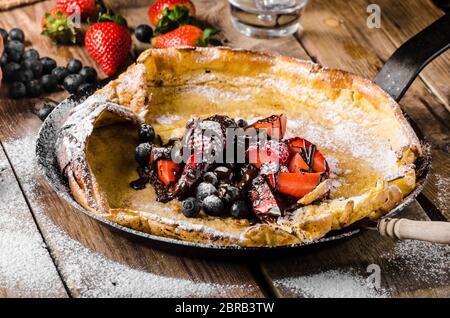 Holländische Baby-Pfannkuchen mit Beeren und Schokolade, gebacken im Ofen auf Eisenpfanne, besten Pfannkuchen immer!!! Stockfoto