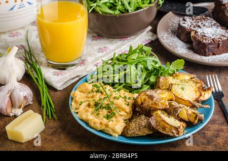 Knusprige zerschlagen Kartoffeln, Rührei und kleinen Salat, Saft und Kuchen zum Frühstück Stockfoto