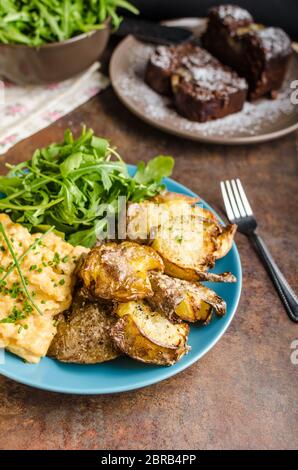 Knusprige zerschlagen Kartoffeln, Rührei und kleinen Salat, Saft und Kuchen zum Frühstück Stockfoto