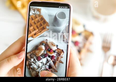 Weibliche Hände fotografieren Teller mit hausgemachten belgischen Waffeln mit Zuckerpulver Stockfoto