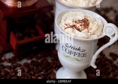 Irish Coffee, eine köstliche Kaffeespezialität mit Schlagsahne in einer extravaganten Tasse, alte Kaffeemühle im Hintergrund Stockfoto