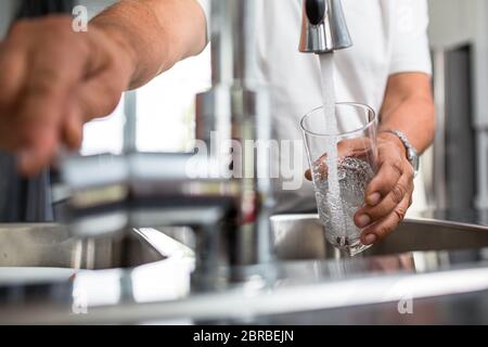 Hände eines älteren Mannes gießen ein Glas Wasser in eine moderne Küche Stockfoto