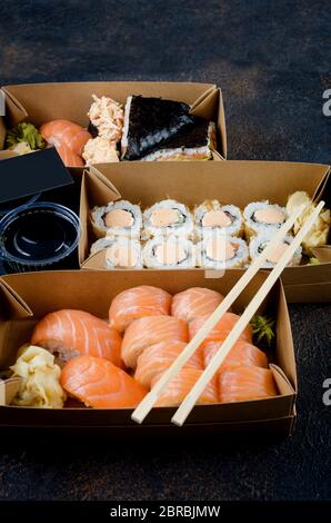 Leckere Sushi-Brötchen in Einweg-Kraftpapier-Boxen, Saucen, Essstäbchen. Sushi zum Mitnehmen oder Anliefern Stockfoto