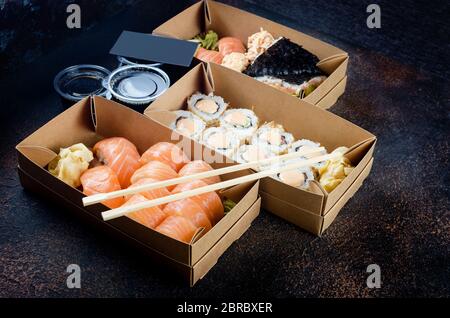 Leckere Sushi-Brötchen in Einweg-Kraftpapier-Boxen, Saucen, Essstäbchen. Sushi zum Mitnehmen oder Anliefern Stockfoto