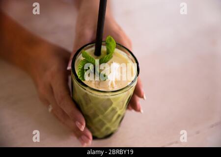 Grüner veganer gesunder Smoothie mit Minze in Glas in weiblichen Händen. Sauberes Detox Essen. Gewichtsverlust Konzept Stockfoto