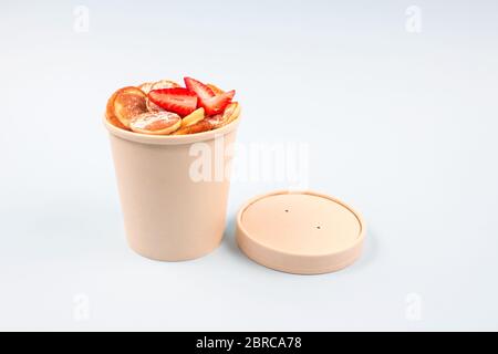 Mini Pfannkuchen Müsli mit Erdbeeren in recycelbaren Pappbecher Verpackung auf hellblauem Hintergrund mit Kopierraum für Ihren Text und Mockup. Trendy Foo Stockfoto