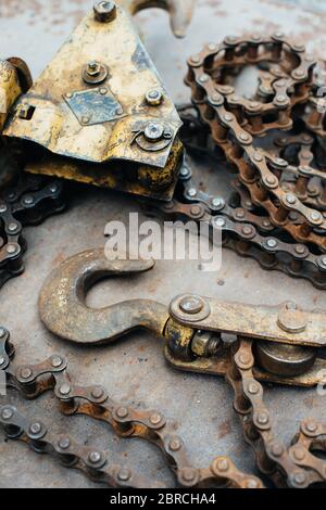 Alte rostige sowjetische selbstgemachte Winde, mit Spuren von gelber Farbe. Haken, Fahrradkette, Kettenglieder. Die Winde liegt auf einem Blech aus rostfreiem Eisen. Metallschrott. Stockfoto