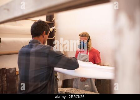 Zwei kaukasische männliche Surfboard Hersteller machen ein hölzernes Surfbrett zusammen und Polieren Stockfoto