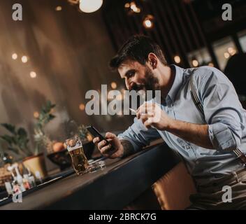 Junger Mann, der Bier trinkt und Zigarette raucht Stockfoto