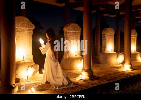 Hue City, Thua Thien Hue Provinz, Vietnam - 7. Mai 2020: Ein Bild eines Mädchens in einem traditionellen AO dai betet in einem Tempel, der von viel Licht umgeben ist Stockfoto