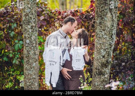 Eine schwangere junge Frau und ihr Mann. Eine glückliche Familie hängend Babykleidung an einem Seil zu trocknen. Schwangere Frau im Park entspannen. Stockfoto