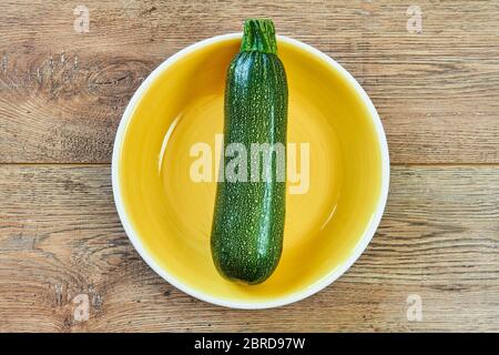 Color Stillleben - gemusterter grüner Zucchini-Kürbis auf gelber Platte auf Holztisch Stockfoto