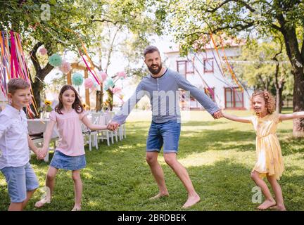 Mann mit Kindern auf Geburtstagsfeier im Garten im Sommer spielen. Stockfoto