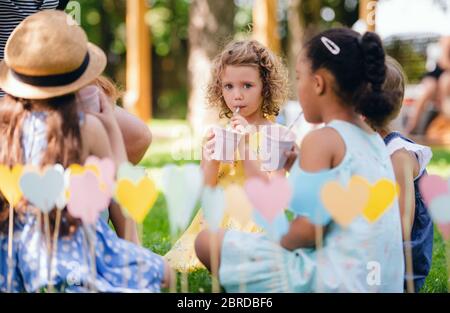 Kleine Kinder sitzen im Sommer draußen im Garten auf dem Boden und trinken. Stockfoto