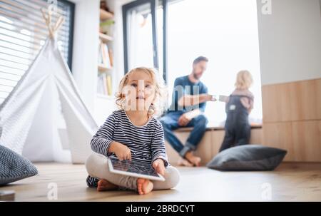 Kleines Kleinkind Mädchen sitzt drinnen im Schlafzimmer, mit Tablet. Stockfoto