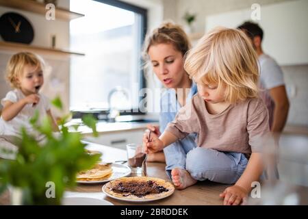 Junge Familie mit zwei kleinen Kindern drinnen in der Küche, Pfannkuchen essen. Stockfoto