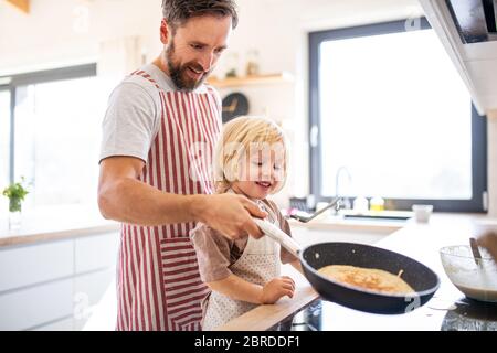 Ein Seitenansicht des kleinen Jungen mit Vater drinnen in der Küche, die Pfannkuchen macht. Stockfoto