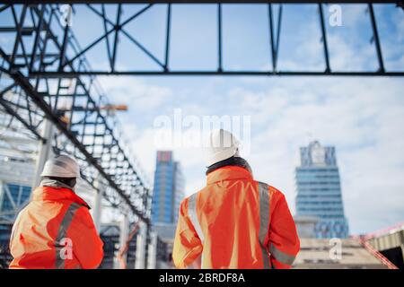Rückansicht der Ingenieure, die auf der Baustelle im Freien stehen. Stockfoto