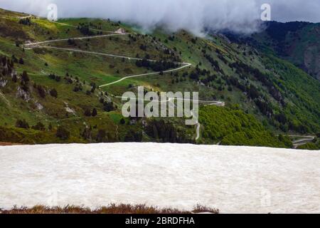 Die Straße schlängelt sich in Richtung Port de Pailhères, Col de Pailhères, über AX les Thermes, Ariege, Französisch Pyrenäen, Pyrenäen, Frankreich. Mit Schnee und Wolken. Stockfoto