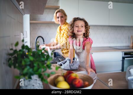 Ein nettes kleines Mädchen mit Mutter drinnen in der Küche zu Hause, Geschirr abwaschen. Stockfoto