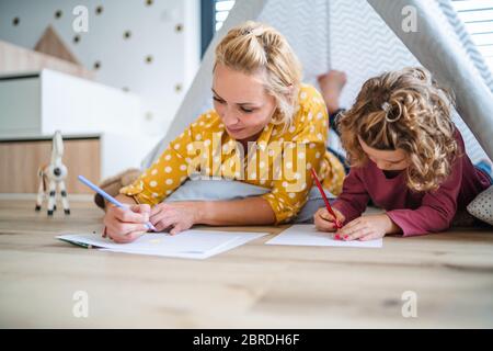 Ein nettes kleines Mädchen mit Mutter drinnen zu Hause, Bilder zeichnen. Stockfoto