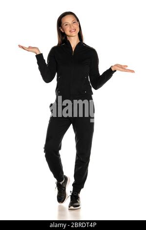 Junge lächelnde Frau in schwarzem Track Suit, die imaginäre Objekte in ihren Händen auf weißem Hintergrund hält Stockfoto