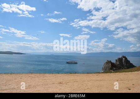 Blick auf den Schamanen-Felsen auf der Insel Olchon mit einem Kreuzfahrtschiff auf dem Wasser in der Nähe (Baikalsee, Russland) Stockfoto