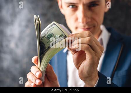 Mann Geschäftsmann in einem Anzug hält einen Stapel von hundert-Dollar-Rechnungen in seinen Händen, zeigt es pompös. Das Konzept des Erhaltens und des Erhaltens eines großen morgens Stockfoto