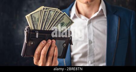 Mann Geschäftsmann in einem Anzug hält einen Stapel von hundert-Dollar-Rechnungen in seinen Händen, zeigt es pompös. Das Konzept des Erhaltens und des Erhaltens eines großen morgens Stockfoto