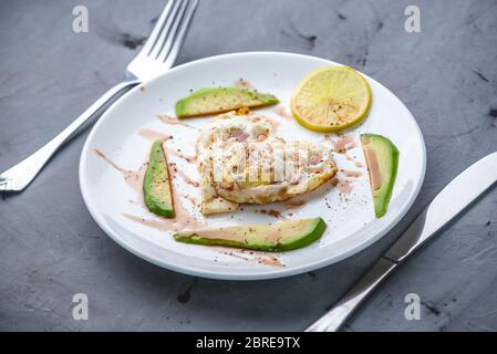Ein schönes gesundes romantisches Frühstück mit Spiegeleiern in Form eines Herzens mit Scheiben Avocado und Zitrone auf einem weißen Teller. Stockfoto